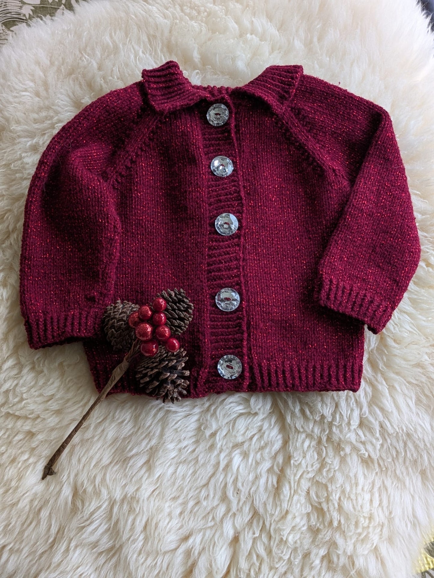 Red knitted cardigan with decorative elements on a white fluffy surface